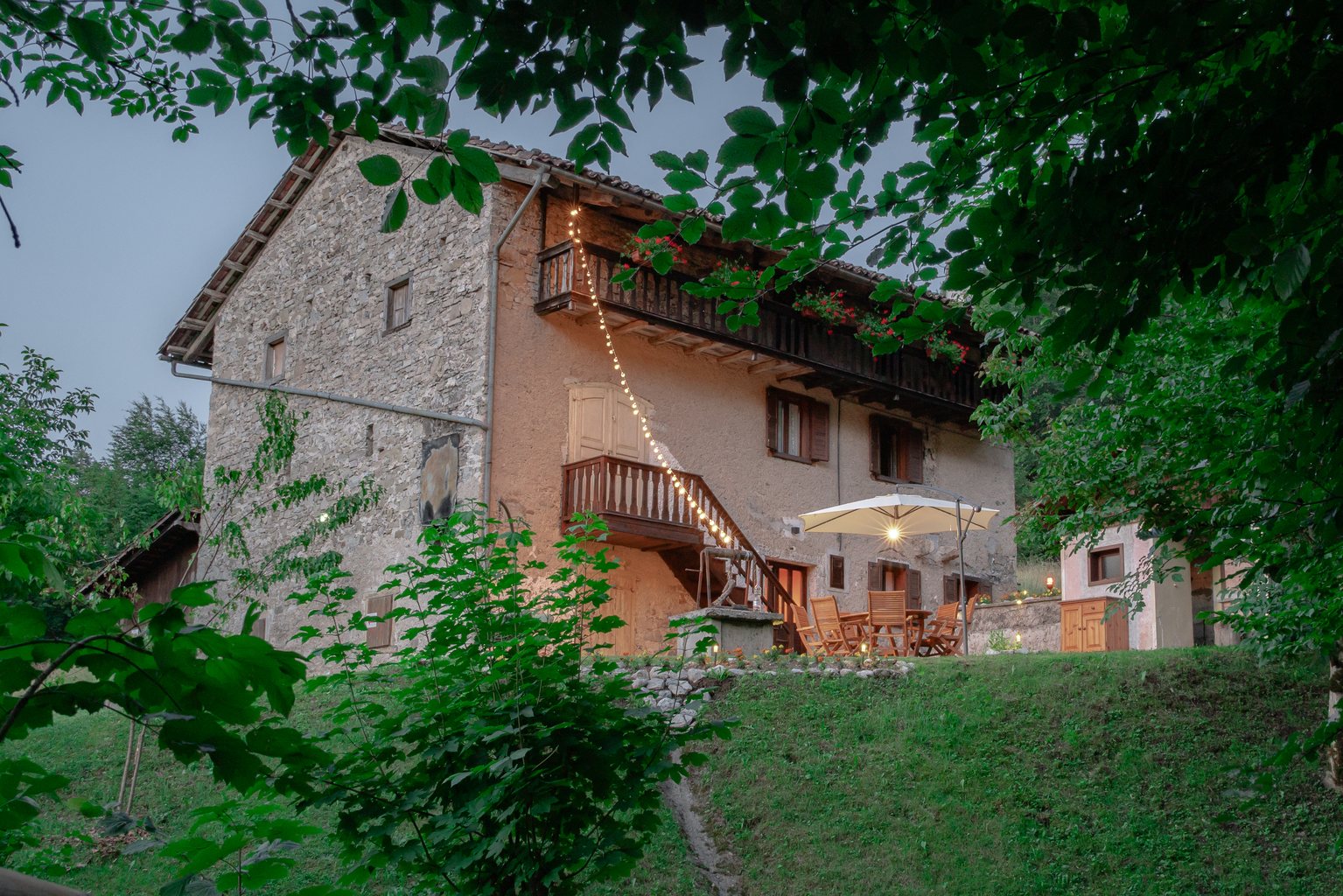 Esterno serale dello chalet Wooden Stories illuminato tra il bosco